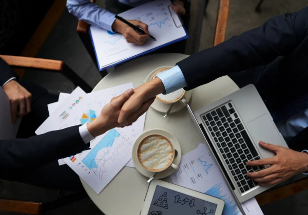 Two people handshaking over the table with charts and coffee cups because of positive result of OpenSolar Integration